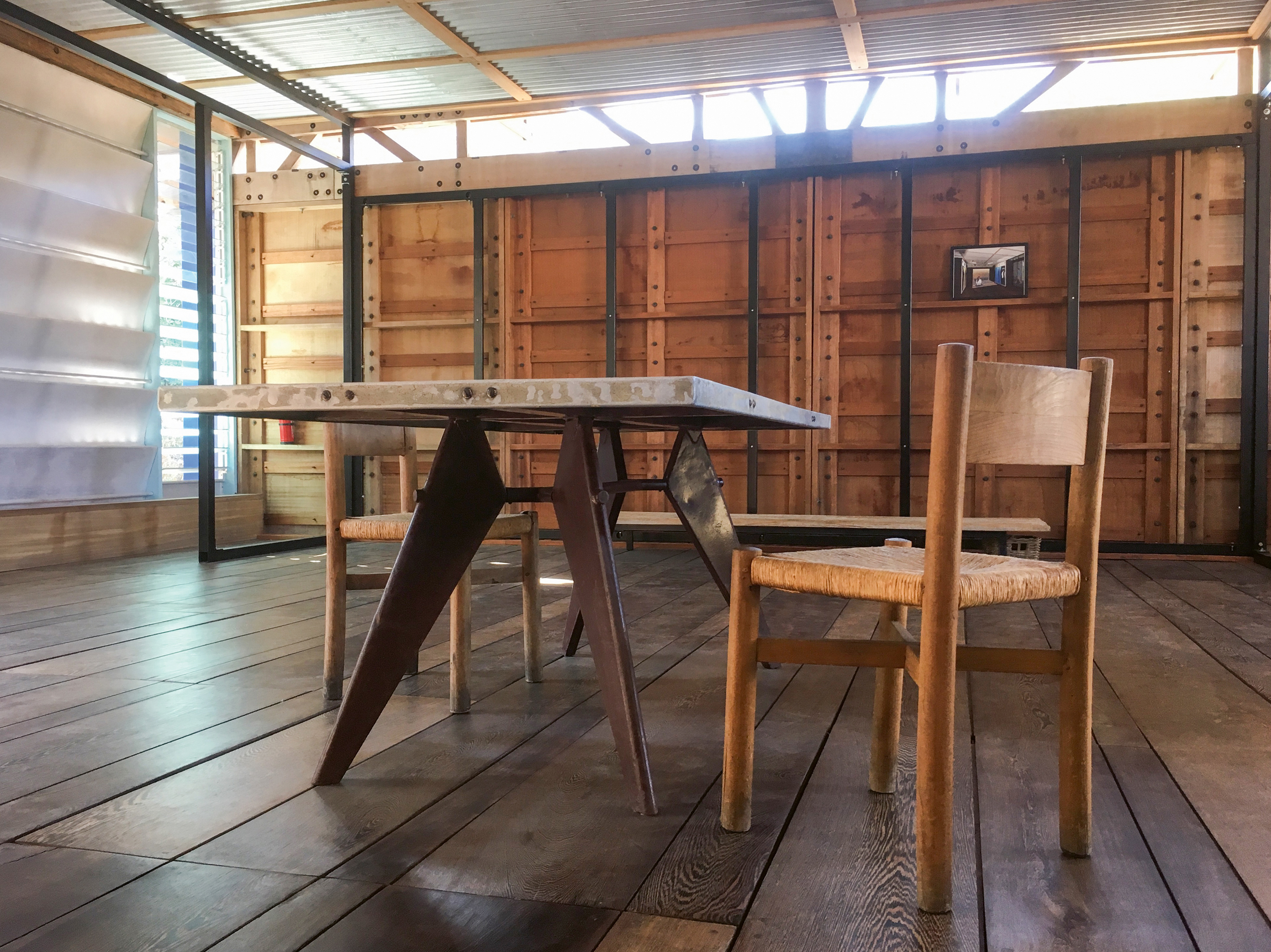 Der Pavillon Cameroun von Jean Prouvé: Die Eckfenster, die gelochten Aluminiumpaneele und das Vordach  sorgen für optimale Durchlüftung und ein angenehmes Innenraumklima. Im Vordergrund stehen ein Tisch von Prouvé und zwei Stühle von Charlotte Perriand.