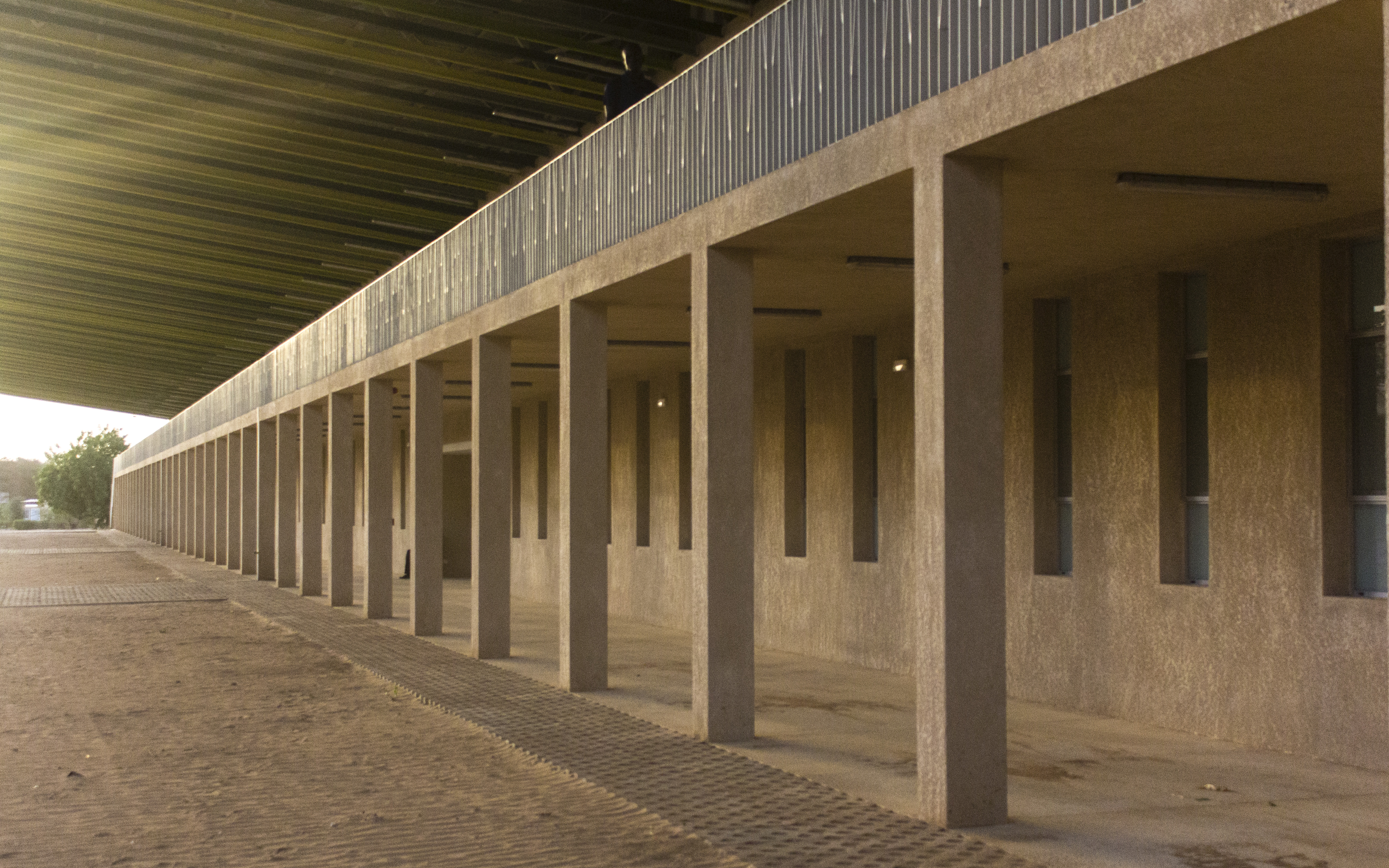 The ramp and stairs lead to an exterior corridor, supported by a row of square pillars, connecting the upper level’s different spaces.