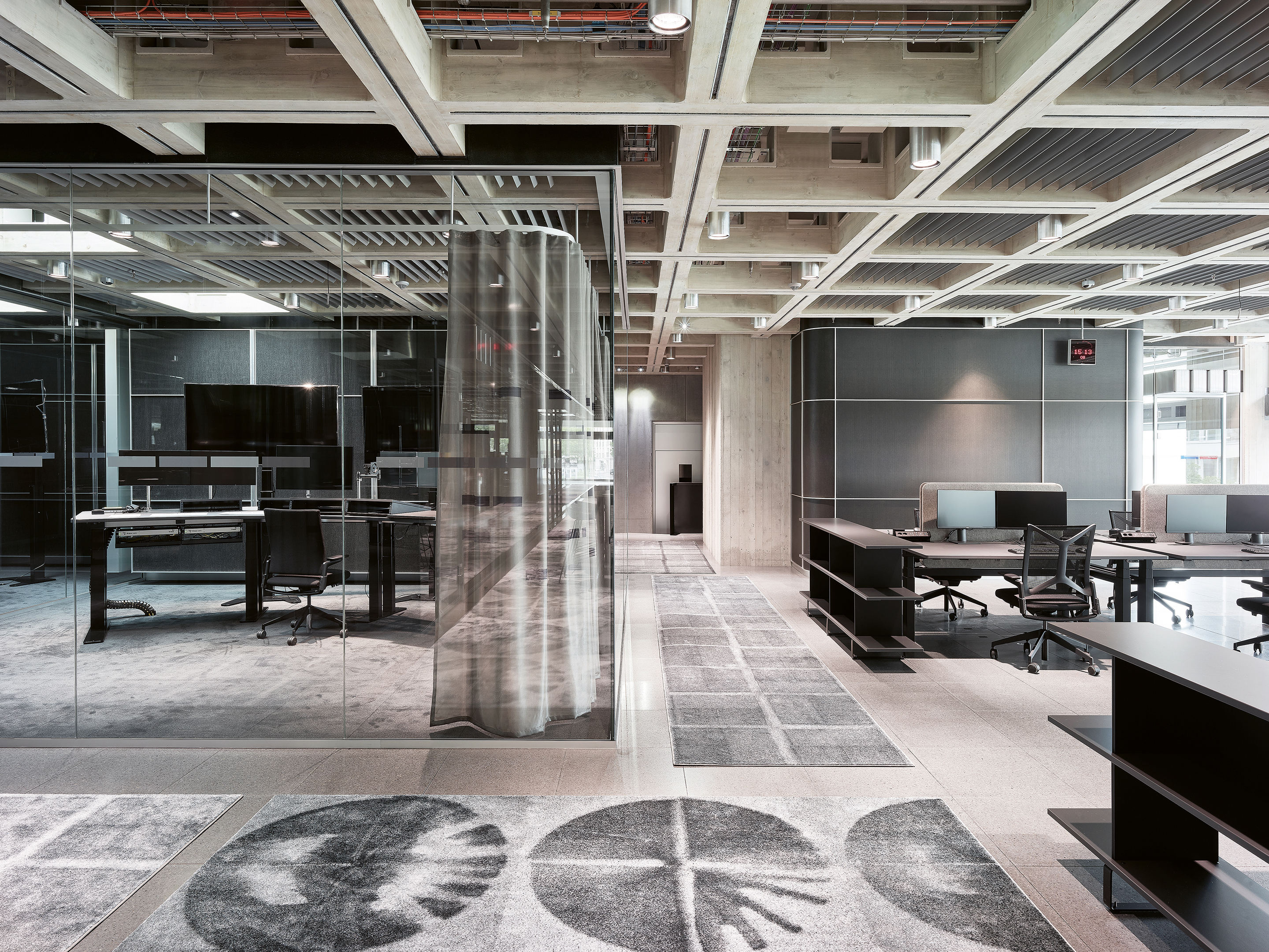 Blick ins 1. OG (Mezzanin)   – die Kunst liegt am Boden: Die Teppiche entstanden in Zusammenarbeit mit dem Künstler Tobias Hantmann. Die Decke ist wie im EG als Kassettendecke aus Ortbeton ausgebildet, die Leitungen sind sichtbar.