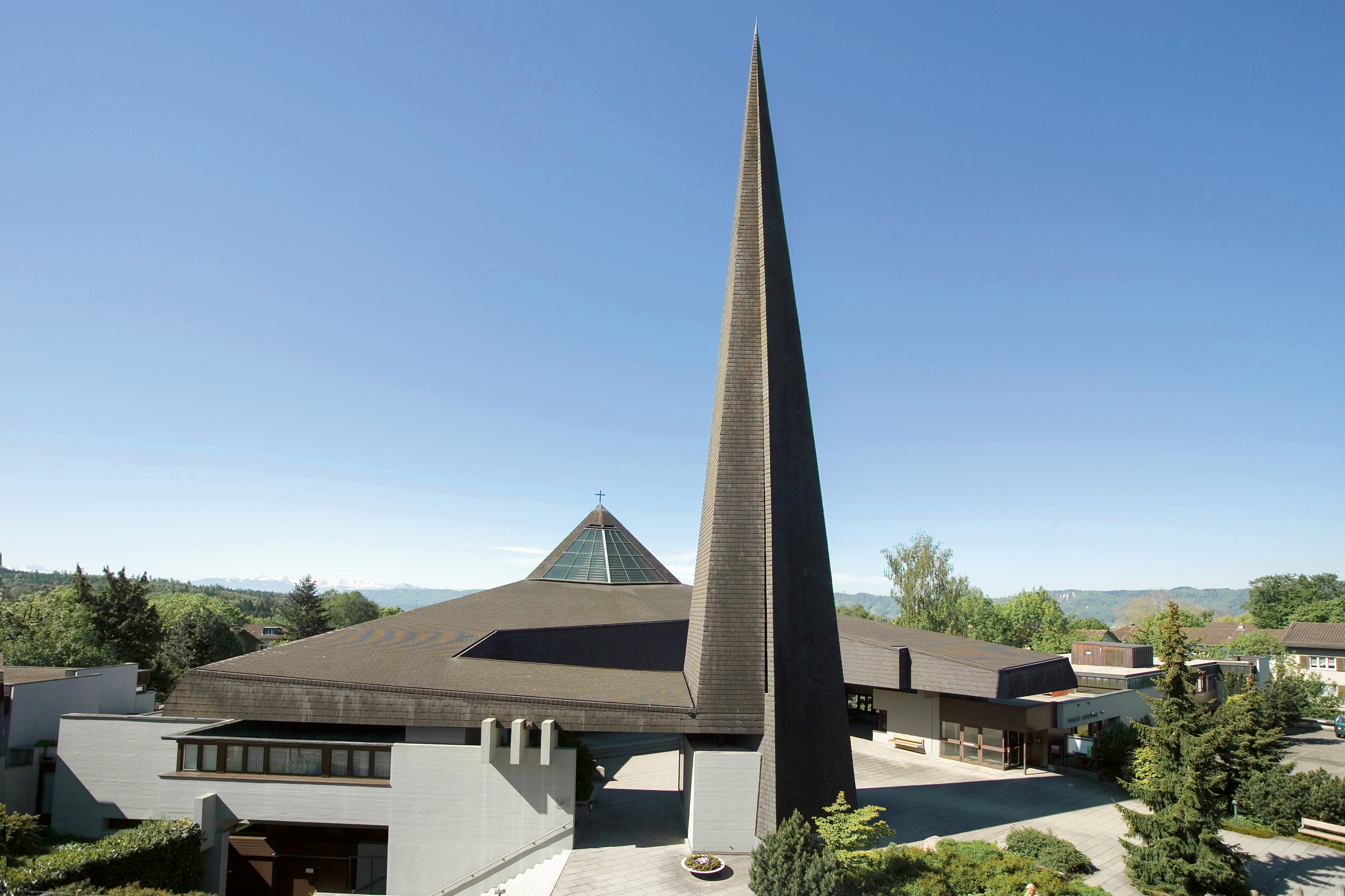 Katholische Kirche Maria Krönung in Zürich Witikon: Wie ein Band, das an der Kirchturmspitze aufgehängt ist, schwebt die Dachhaut über den tragenden Gebäudeteilen. Sie verbindet Pfarrwohnung, Kirche, Vorplatz und Paulus-Akademie zu einem ­baulichen Ensemble.