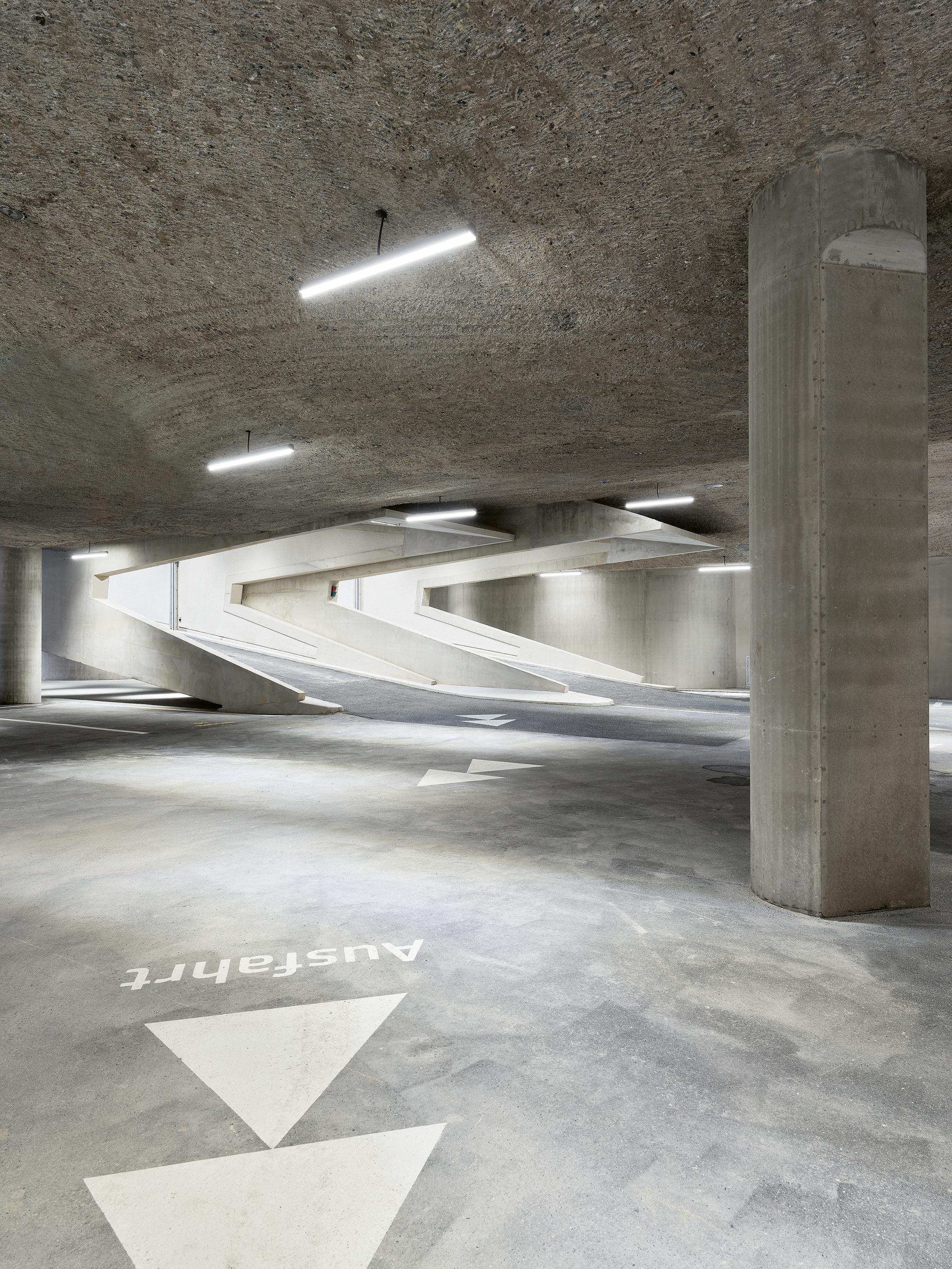 Blick ins  1. UG: Die Zufahrten der Tiefgarage erinnern an die Tunnelportale der Gotthardautobahn. Die Öffnungen in der Decke leiten das Tageslicht ins Innere. Gut erkennbar sind  die Kratzspuren des Baggers auf der Deckenuntersicht.