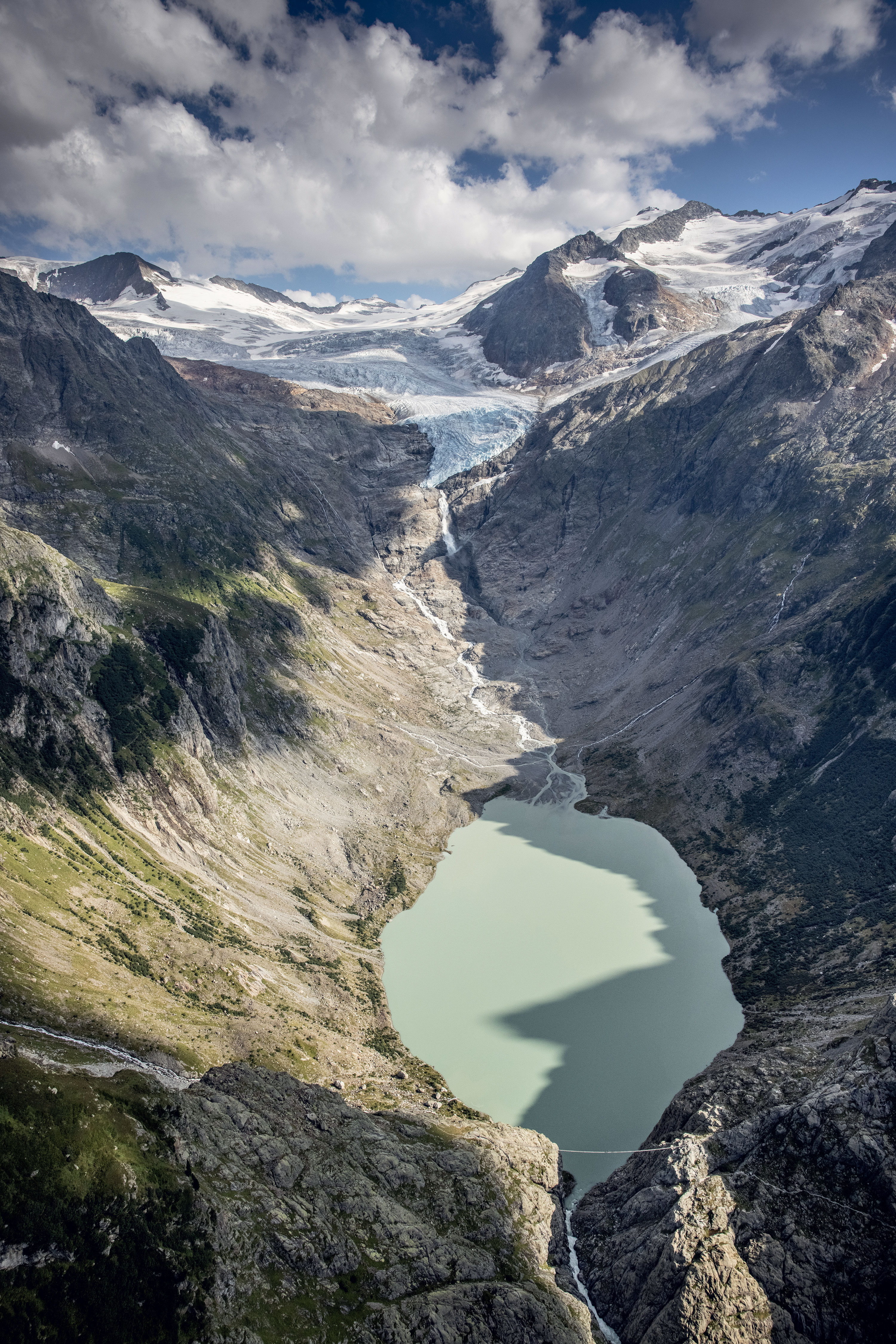 Lac du Trift (BE). Dans les années 1950, le glacier allait jusqu’au bas de la photo. Suite à son recul, un lac de surcreusement est apparu au cours des années 1990. Les Forces motrices de l’Oberhasli souhaitent ériger un barrage au niveau de la passerelle suspendue franchissant le verrou glaciaire afin de rehausser le lac en vue de son exploitation hydroélectrique. Dans son ensemble, le projet produirait 145 GWh/an.