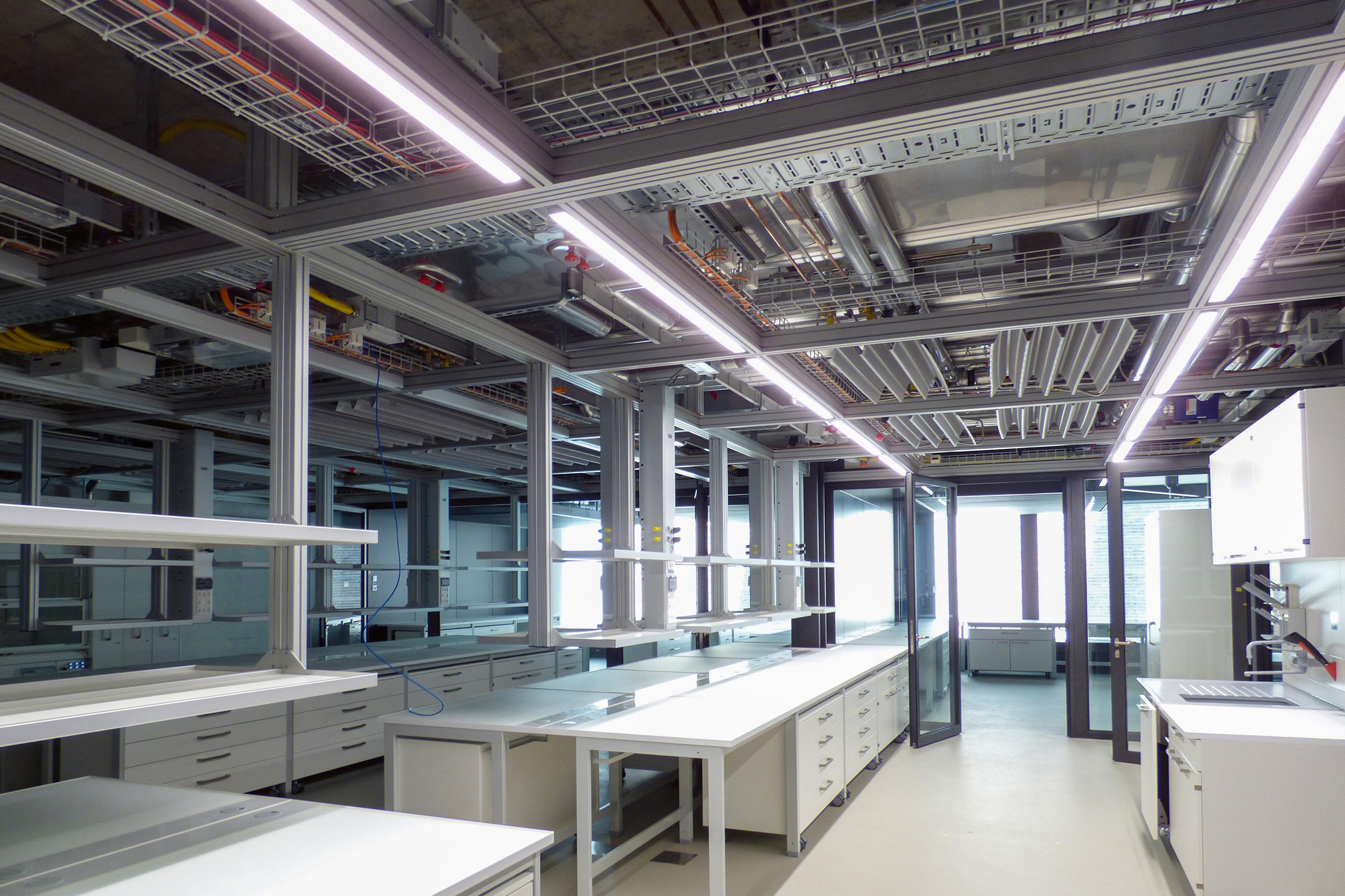 Je tiefer man ins Gebäude eindringt, desto mehr öffnet sich die Gebäudetechnik respektive die Leitungsführung. Ist sie in der Eingangshalle noch verborgen, zeigen sich in den Fluren an der Decke schon punktuelle Technikelemente. In den Laboren sieht man die Leitungen an der Decke.