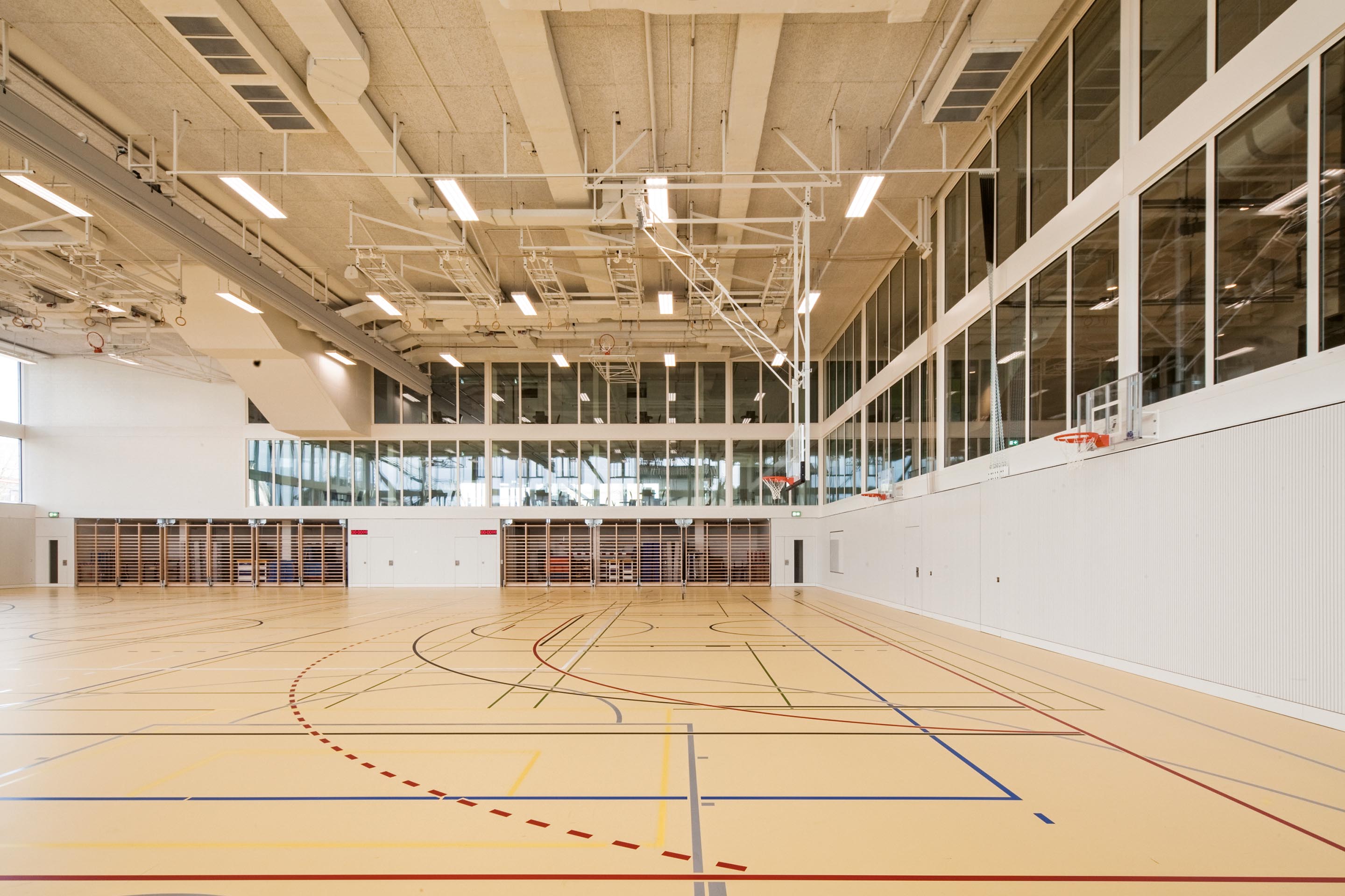 Die Doppelturnhalle erstreckt sich in ihrer Höhe über drei Geschosse und ist von der doppelgeschossigen Aula im EG und den  Nutz- und Verkehrsflächen im 1. Obergeschoss einsehbar. Darüber liegen die Unterrichtsräume und die Lernlandschaft im 2. OG.