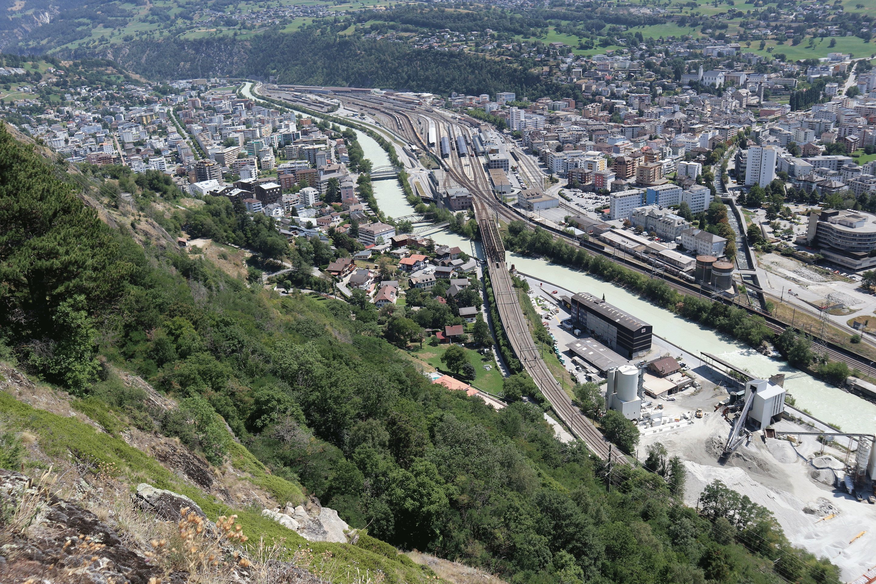 Blick auf Naters (links von der Rhone) und Brig. Im Vordergrund der Wald, der den letzten Abschnitt der Bahnstrecke schützt.