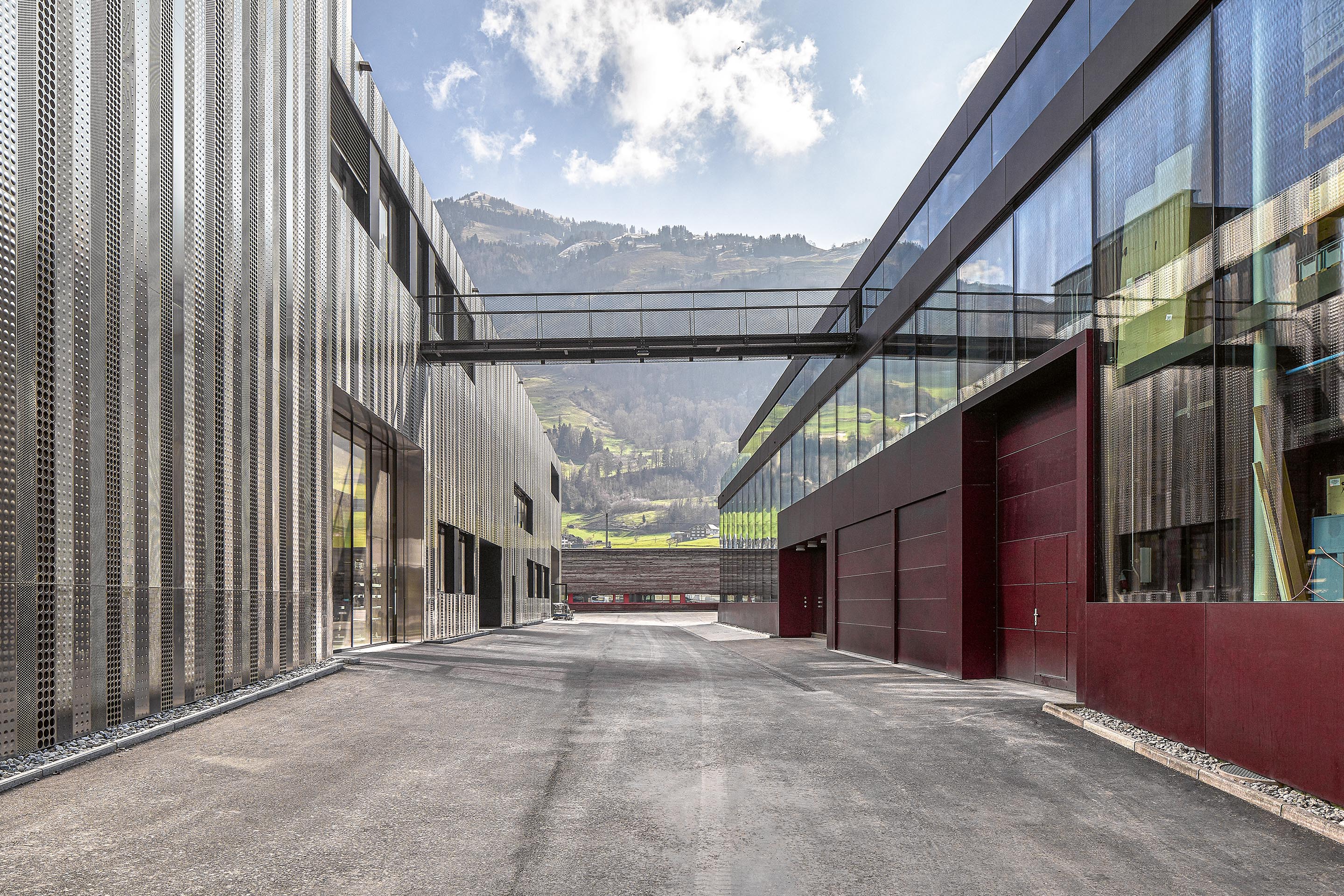 Eine luftige Passerelle verbindet das weinrote Werksgebäude  von 2012 mit dem in Edelstahl gehüllten Neubau von 2020.