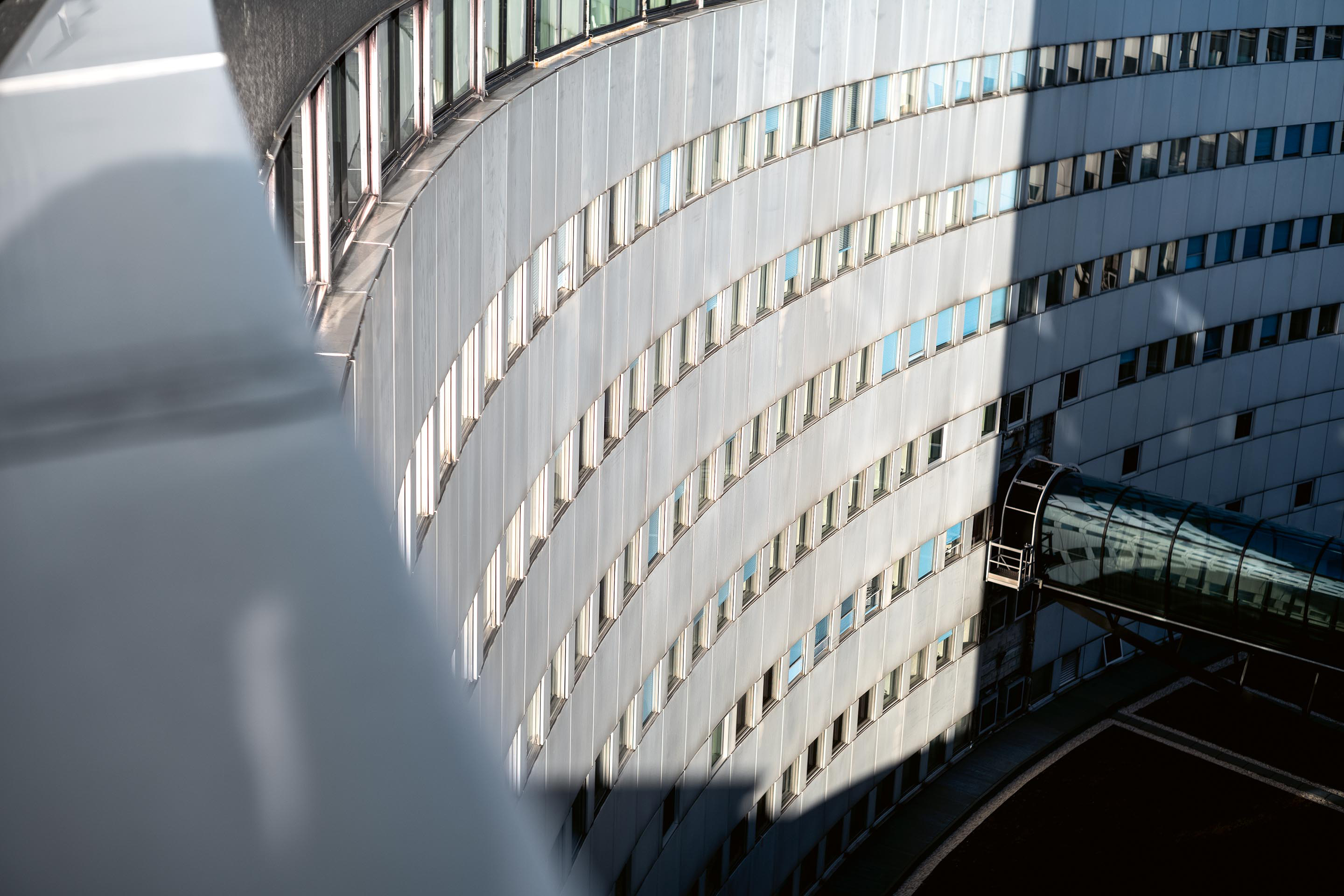 Für die Abfolge der 2400  Fenster der Ringfassade hatte sich Henry Bernard von den Perforierungen einer Diafilmrolle inspirieren lassen. Jedes Fenster lässt sich über eine Handkurbel an der Wand öffnen und die Fassadenpaneele sind aus 4 mm dickem Aluminium.