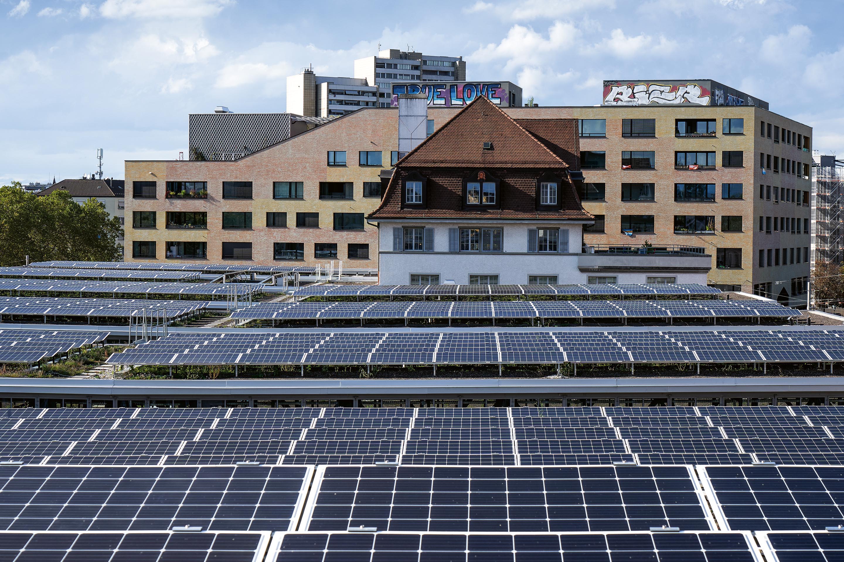 Nachhaltiges Bauen mit geringer CO2-Emission im Gefüge einer Stadt: Der Blick vom Tramdepot Elisabethenstrasse  zeigt unterschiedliche Ansätze für die Reduktion von Treibhausgasen wie die lokale Nutzung von Solarenergie oder  eine Optimierung der Ressourceneffizienz bei der Genossenschaftssiedlung Kalkbreite (gelbes Gebäude in der Bildmitte).