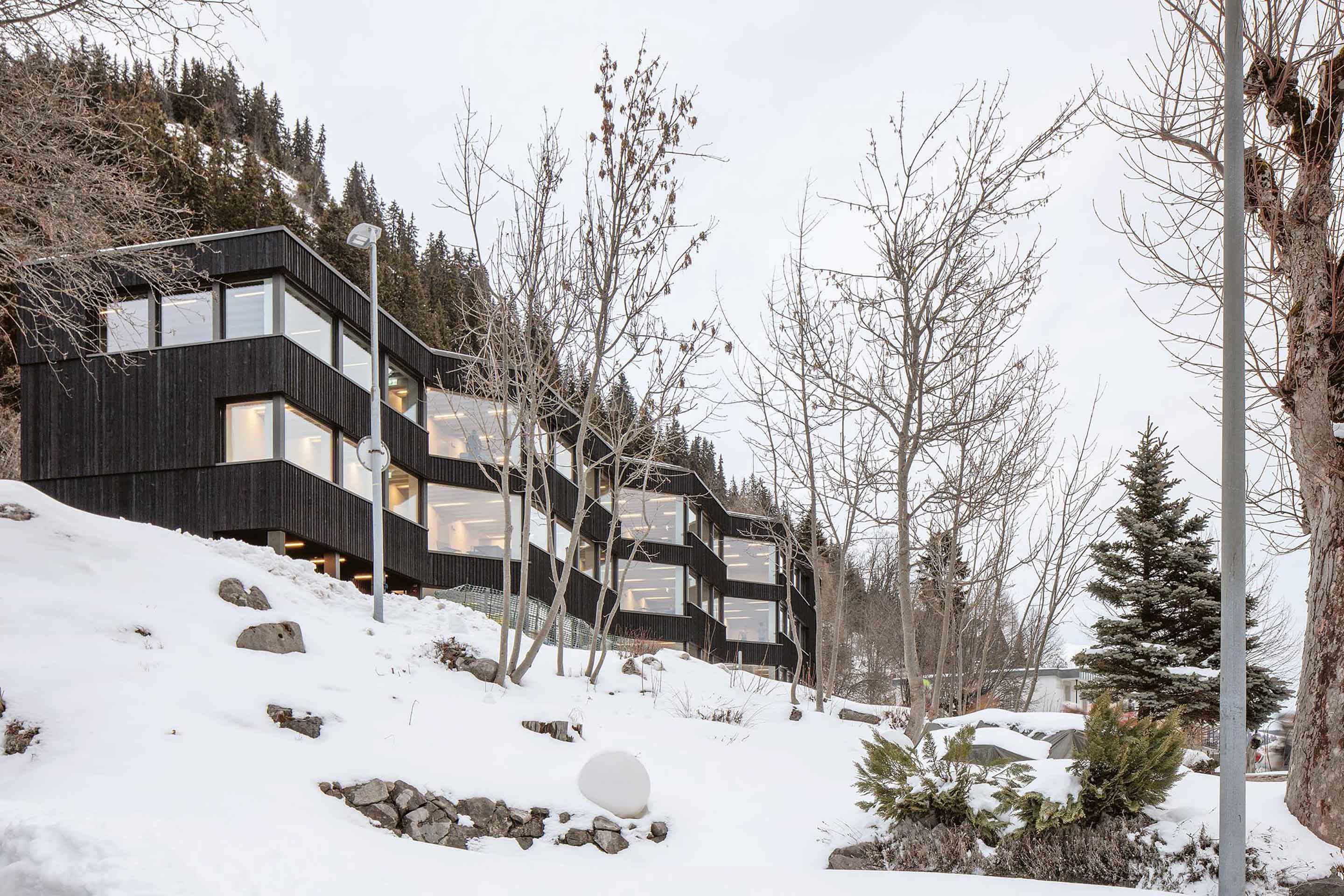 Il centro didattico alpino di meier + associés architectes estende i suoi spazi comuni in un lungo corridoio vetrato che attraversa la larghezza del lotto.