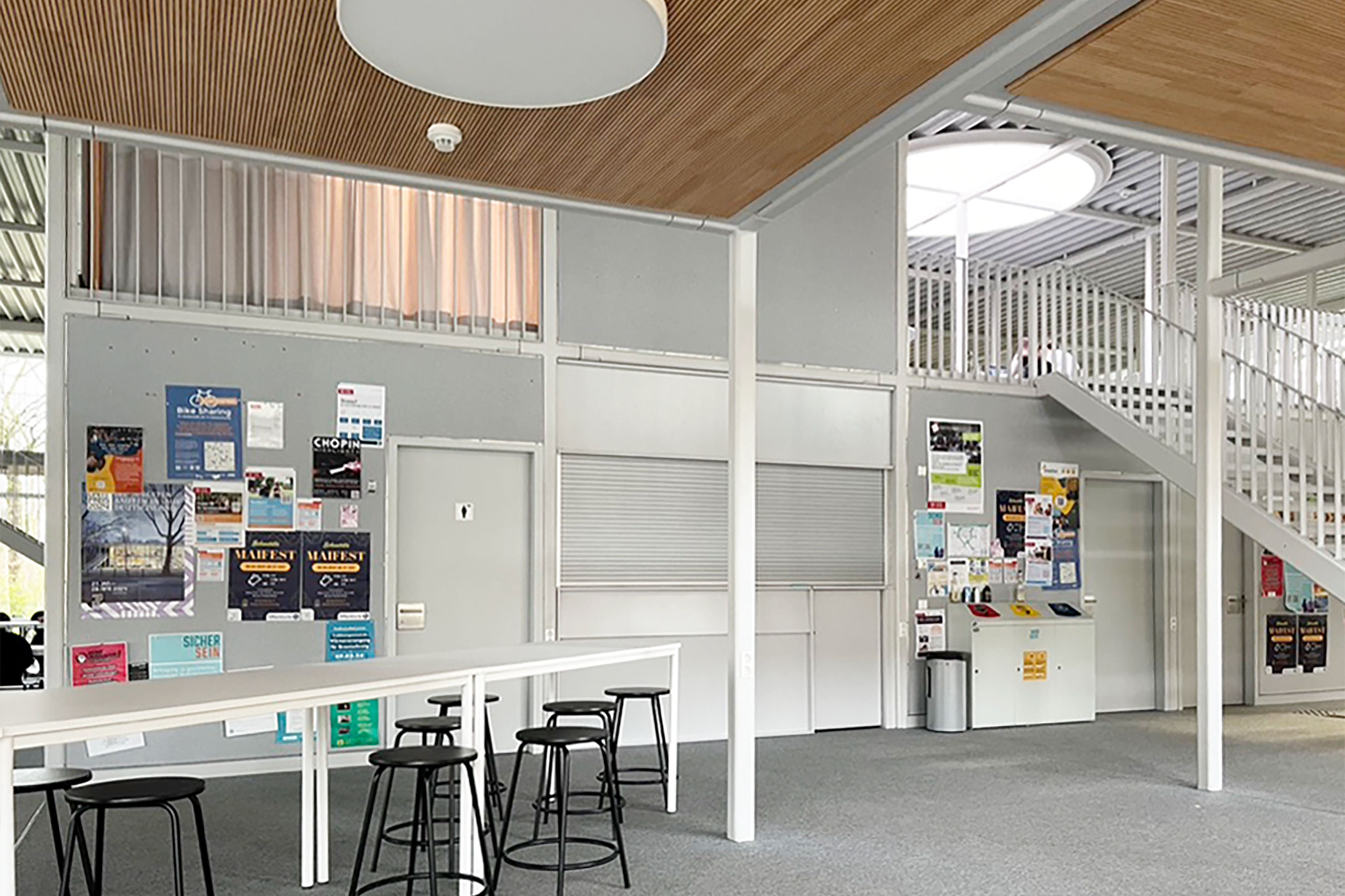 Le bar situé dans le noyau du bâtiment est encore en attente d’un projet d’exploitation émanant du corps étudiant. En plus d’intervenir dans l’isolation acoustique, les panneaux muraux servent de panneaux d’affichage.