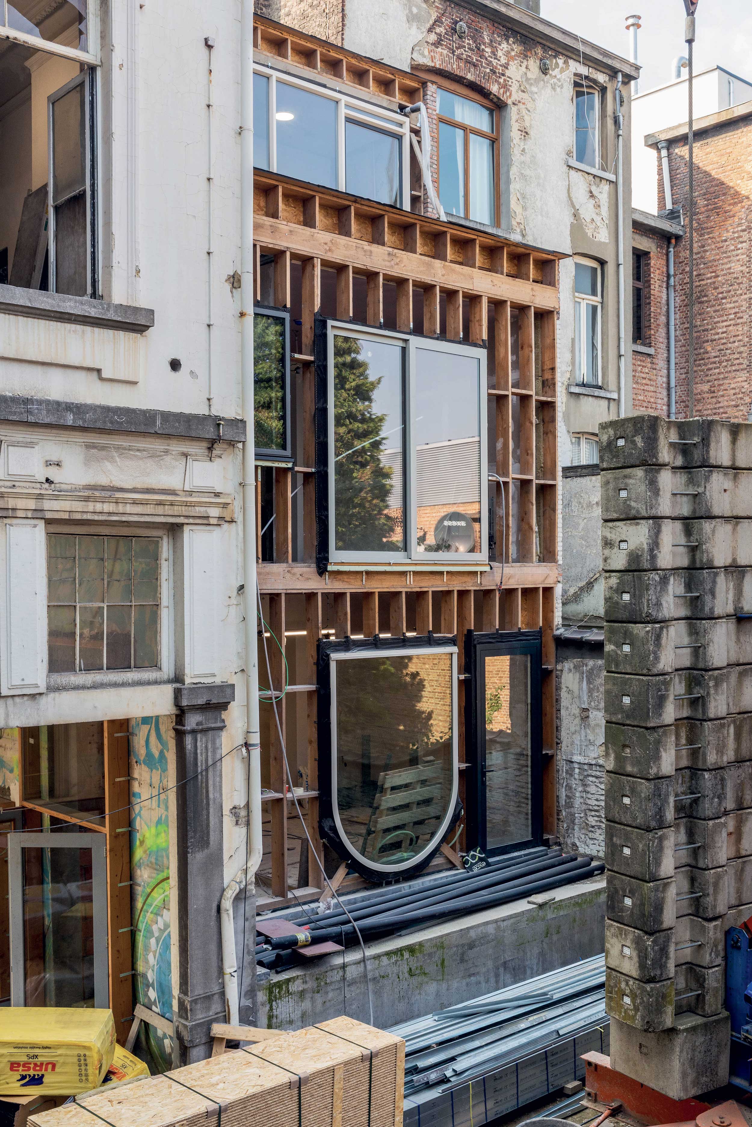 Photographie de la façade de Zinneke prise en 2020 pendant le chantier, les fenêtres issues du réemploi sont disposées pour former une nouvelle composition-manifeste.