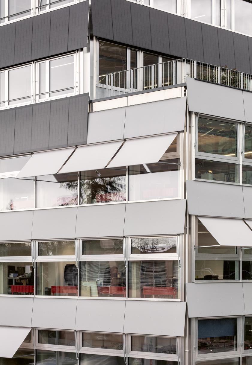 Staggered façades, structural lightness, and the inclination of panels and sunshades disrupt the building’s apparent neutrality.