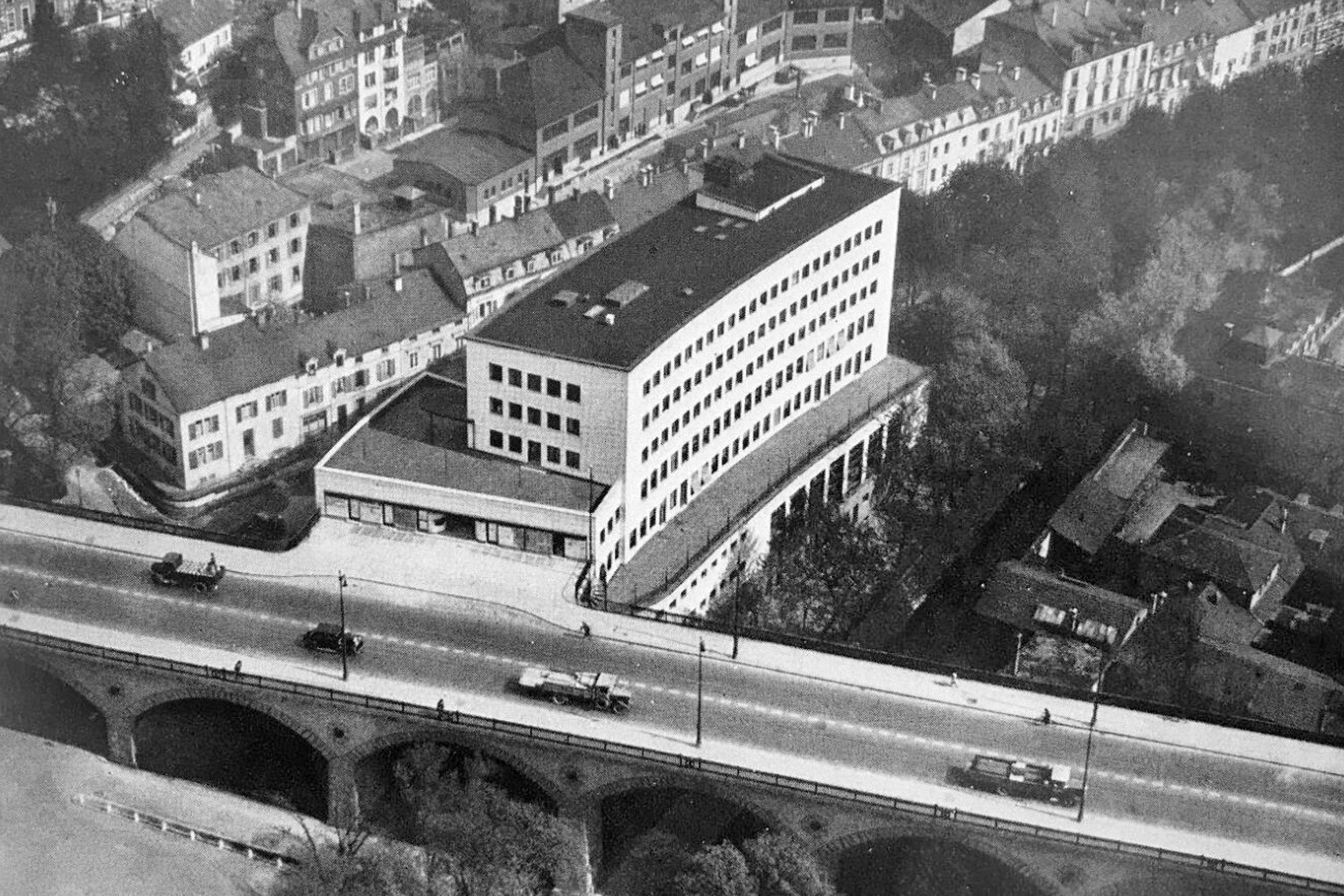 The historical image shows the Rialto indoor swimming pool from the south. To the left of the building, Birsigstrasse runs under the viaduct. On the right, the Birsig river flows through the Nachtigallenwäldeli forest.