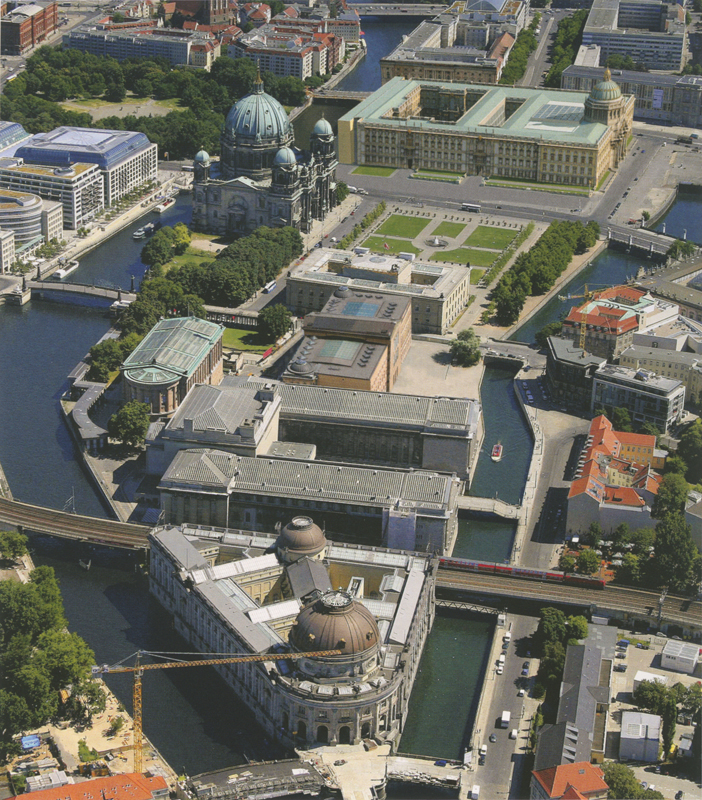 Überblick: Luftaufnahme der Museumsinsel in Berlin, wie sie sich heute präsentiert – ein Ensemble eigenständiger Solitärbauten verschiedener Epochen, die über Kolonnaden, Hochkorridore und gestaltete Freiflächen zu einer Einheit verbunden sind.