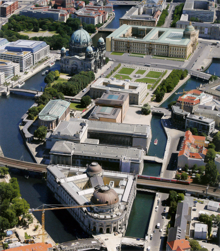 Überblick: Luftaufnahme der Museums­insel in Berlin, wie sie sich heute präsentiert: ein Ensemble eigenstän­diger Solitärbauten verschiedener Epochen, die über Kolonnaden, Hochkorridore und gestaltete Freiflächen zu einer Einheit verbunden sind.