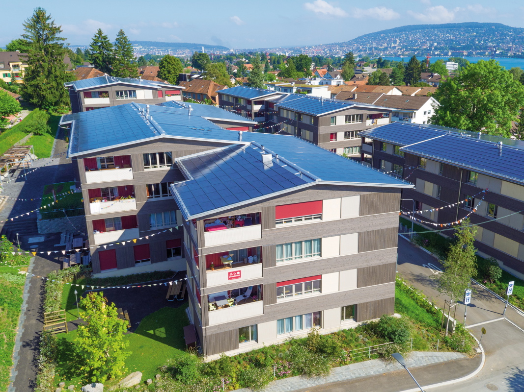 Erstplatzierte des mittlerweile zum siebten Mal verliehenen Norman Foster Solar Award ist eine Wohnsiedlung in Zürich. Die Neubauten haben eine unauffällige, schlichte Holzfassade und für dieses Quartier typische Giebel­dächer. Im Gegensatz zu den Nachbarn sind diese aber mit integrierten monokristallinen PV-Zellen gedeckt.