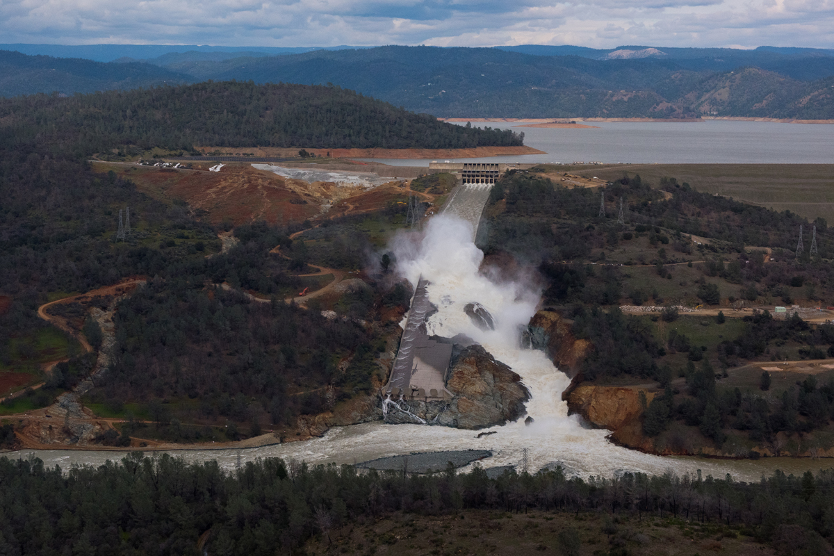 Luftansicht des Lake Oroville: Links ist derjenige Teil des Damms erkennbar, der als Überlauf ausgebildet ist, der Hang darunter ist teilweise stark erodiert. In der Bildmitte die Hochwasser-Notentlastung mit beschädigter Schussrinne.