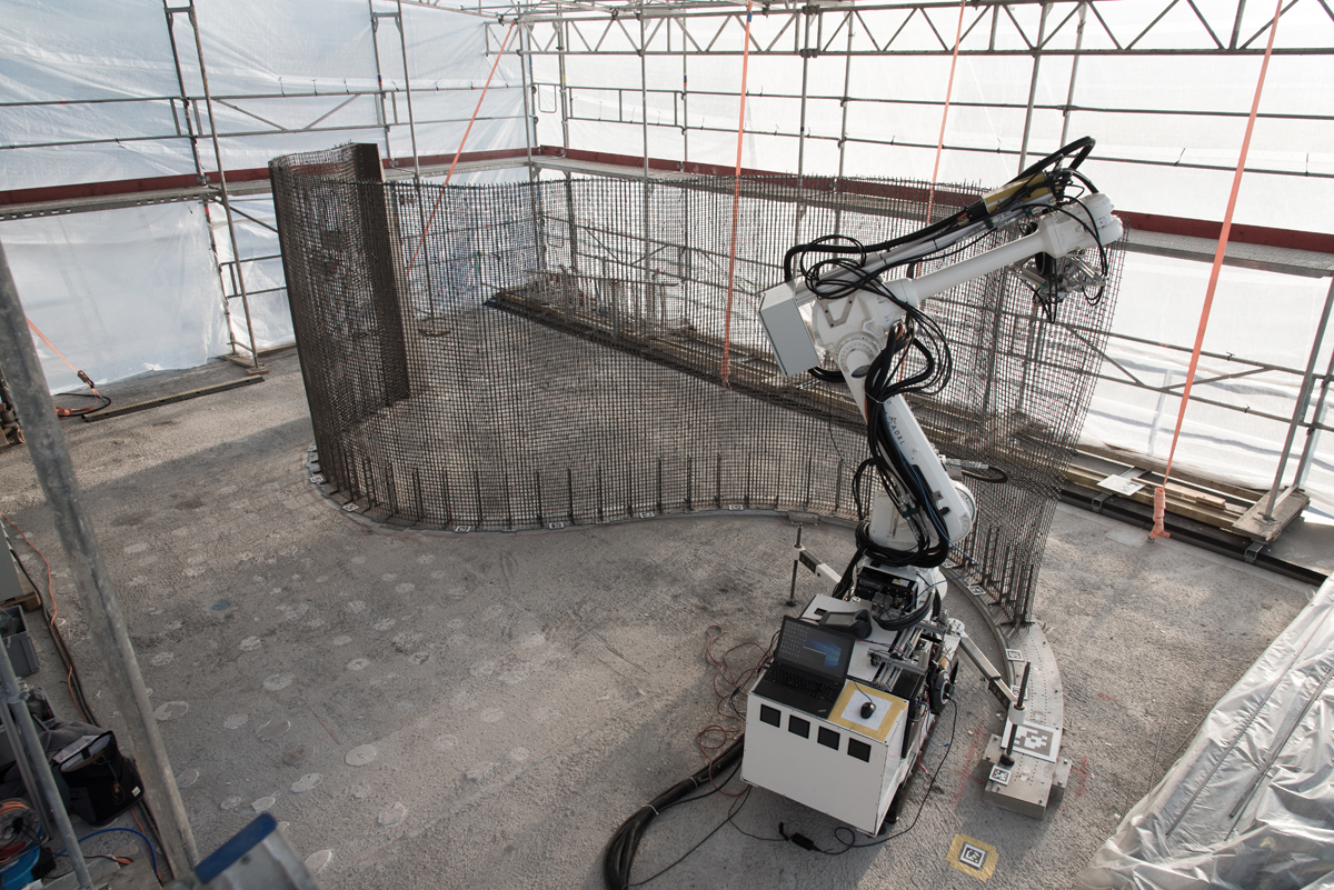 Der Bauroboter «In situ Fabricator» baut mithilfe der «Mesh Mould»-Technologie ein Stahldrahtgitter im Forschungsgebäude NEST. Mesh Mould kombiniert die beiden Funktionen Schalung und Bewehrung des Betons in einem Stahldrahtgitter. Die Fertigung einer Wand geschieht in einem einzigen von Robotern kontrollierten Prozess.