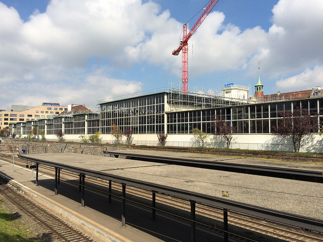 Blick nach Süden über den Einschnitt der SBB-Seebahnlinie nach Aussersihl: Das Denkmal geschützte Tramdepot (Architekt und Stadtbaumeister Hermann Herter; 1949) muss instand gesetzt und saniert werden. Inwendig wird eine neue Wärmehaut eingebaut; Dach und Oblichter werden energetisch eingepackt und teilweise mit Solarpanels versehen. Im Hintergrund die Genossenschaftssiedlung Kalkbreite.