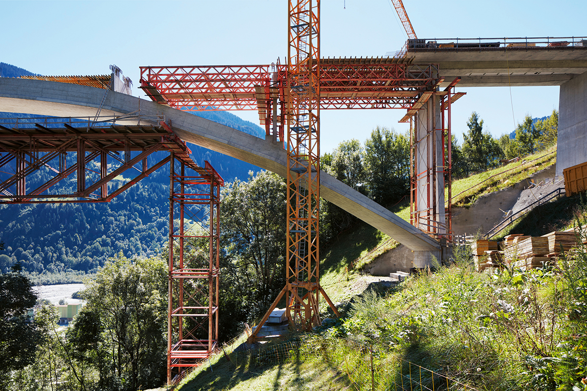 Bauphase der Bogenbrücke mit einfachen Gerüsttürmen und einem verbindenden Fachwerkträger.