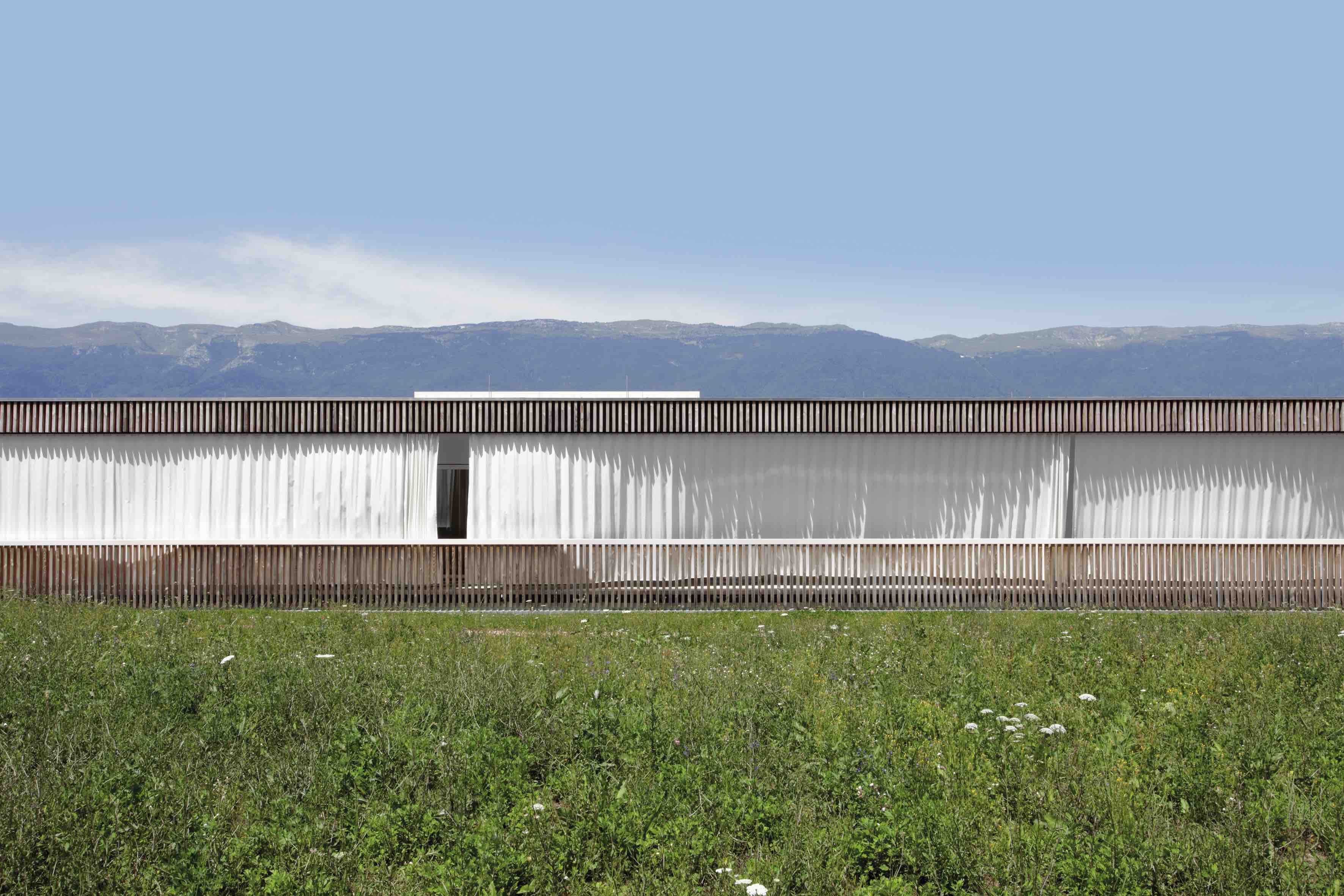 L’edificio, di un solo piano, disegna un nastro orizzontale nel paesaggio circostante con il Giura come quinta.