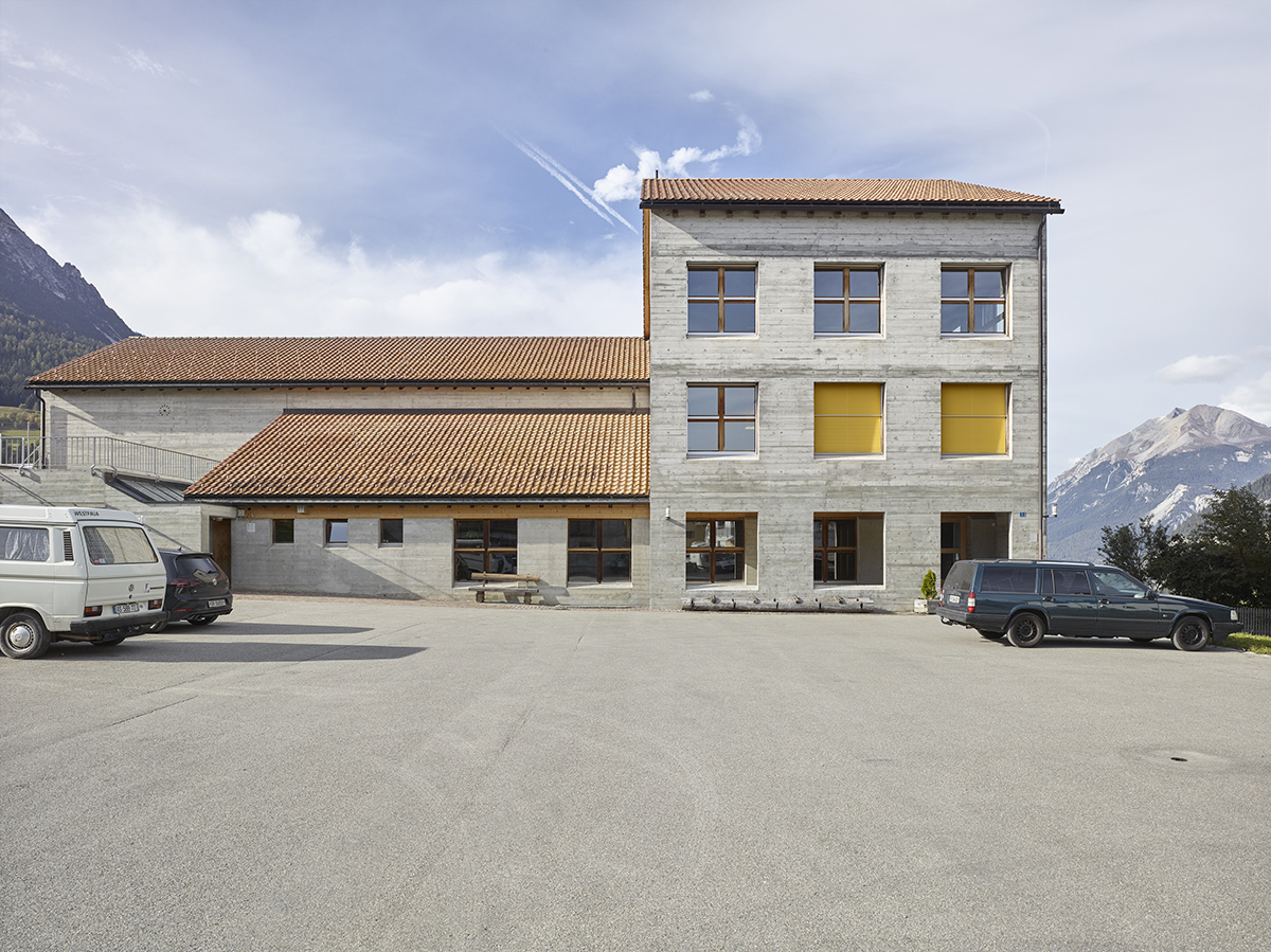 Am nördlichen Dorfrand von Riom befindet sich ein weitläufiger Parkplatz, der zur Landschaft hin von einem Sichtbetonbau abgeschlossen wird: dem 2006 zum Schulhaus erweiterten Mehrzweckbau von 1981/82 (Architektur Monika Brügger (Mehrzweckhalle); Pablo Horváth (Schulhaus)). Heute befinden sich hier Origens Produktionsbüros und die Archive des Festivals. In Zukunft sollen hier Proberäume, Werkstätten, Magazine und Ausstellungsräume entstehen.