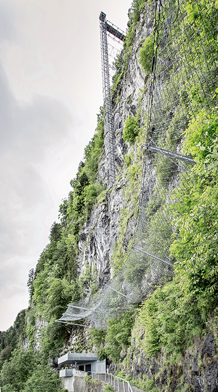 Wie ein provisorisches Gerüst, das über horizontale Verankerungen an den Fels geheftet ist, steht der Aufzugsschacht vor dem Berg,