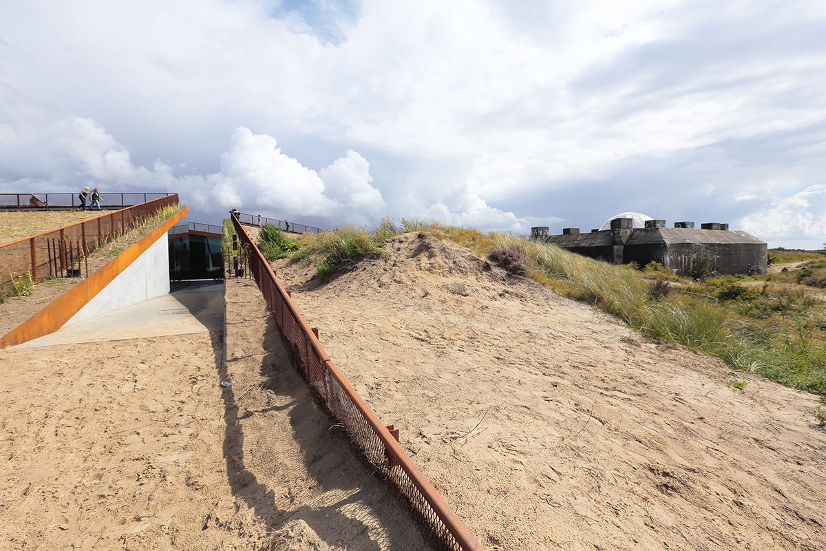 Der Museumsneubau ist unauffällig in die Dünenlandschaft eingefügt. Rechts davon steht weithin sichtbar der deutsche Wehrmachtsbunker.