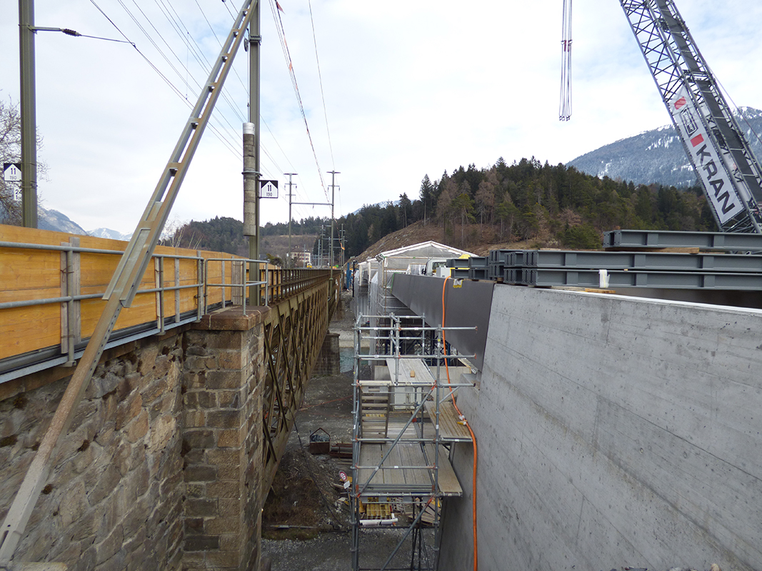Etwa 10 m beträgt der Abstand der beiden Brücken. Die schräg nach innen gestellten, seitlichen Stützwände des stählernen Troges setzen sich aus ästhetischen Gründen im Betonwiderlager fort.