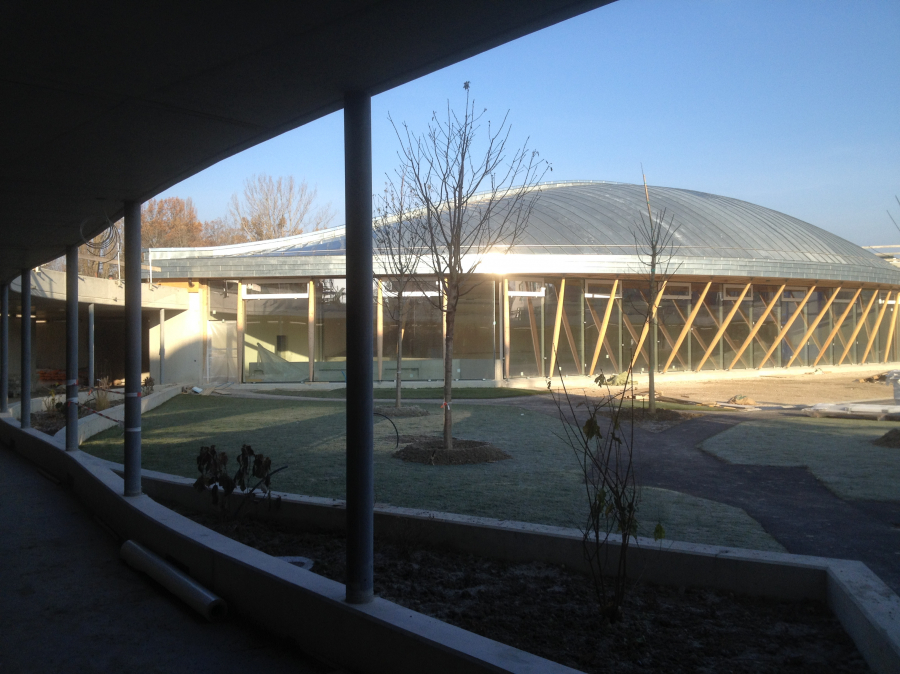 Sporthalle Puplinge GE: Neubau Sportanlage 2014. Erweiterung einer medizinischen Einrichtung mit einer Sporthalle. Die Dachkonstruktion ist einem umgestürzten Boot nachempfunden: mit einem Holzrahmen aus verleimten Brettschichtholzträgern, die alle den gleichen Radius haben und von der Peripherie bis zum Rücken montiert sind. Die Zwischenträgerfüllung besteht aus selbsttragenden MDF-Platten. Bauherrschaft: Schweizerische Eidgenossenschaft; Architektur: KMS Architectes, Genf