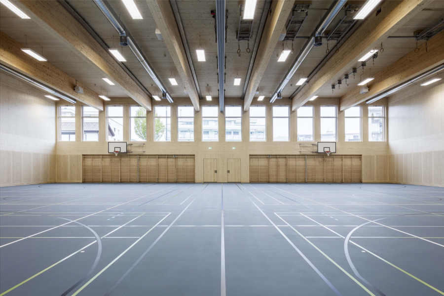 Schulhaus Chrüzacher Bassersdorf ZH: Neubau Turnhalle 2017. Die 28 m breite Turnhalle ist ein reiner Holzbau, mit sechs Hallenträger aus blockverklebtem und einem Flachdach aus Hohlkastenelementen. Bauherrschaft: Gemeinde Bassersdorf; Architektur: Horisberger Wagen Architekten, Zürich
