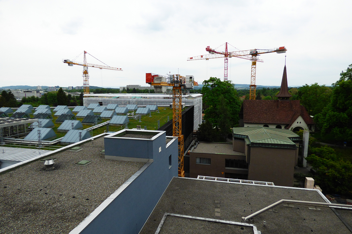 Blick von der Helikopterplattform auf das INO (links), das neuen Organ- und Tumorzentrum (hinten, eingerüstet) und die Klinikkapelle (rechts). Der neue Verbindungsgang liegt entlang der Hausflucht des INO, unterhalb des vordersten Krans.