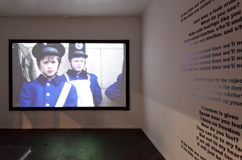 Characters with Unknown Power, 2018 de Rico Scagliola &amp; Michael Meier, catégorie ART L’accès physique à l’installation du duo d’artistes Rico Scagliola &amp; Michael Meier, Characters with Unknown Power, se fait par un passage particulièrement étroit. Au coeur de l’oeuvre se trouve une vidéo projetée sur une paroi dans laquelle défilent des images d’enfants vêtus de costumes traditionnels ou populaires à l’occasion de deux fêtes populaires. Etonnamment passifs, ces enfants attendent, joue