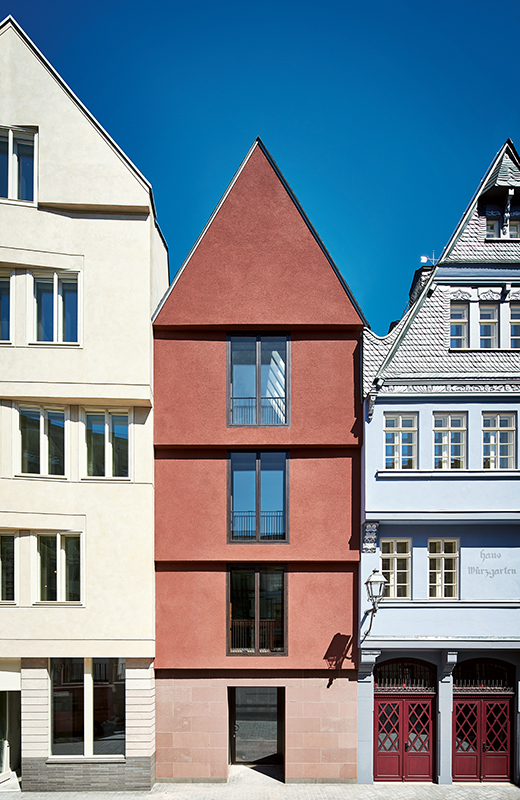 Die Fassade des Neubaus von Morger Partner ist mit Sandstein und rotem Kratzputz versehen. Westseitig grenzt das Gebäude an einen Neubau von Tillmann Wagner Architekten, ostseitig an die Rekonstruktion des Hauses «Würzgarten» aus dem 16. Jahrhundert von Denkmalkonzept.