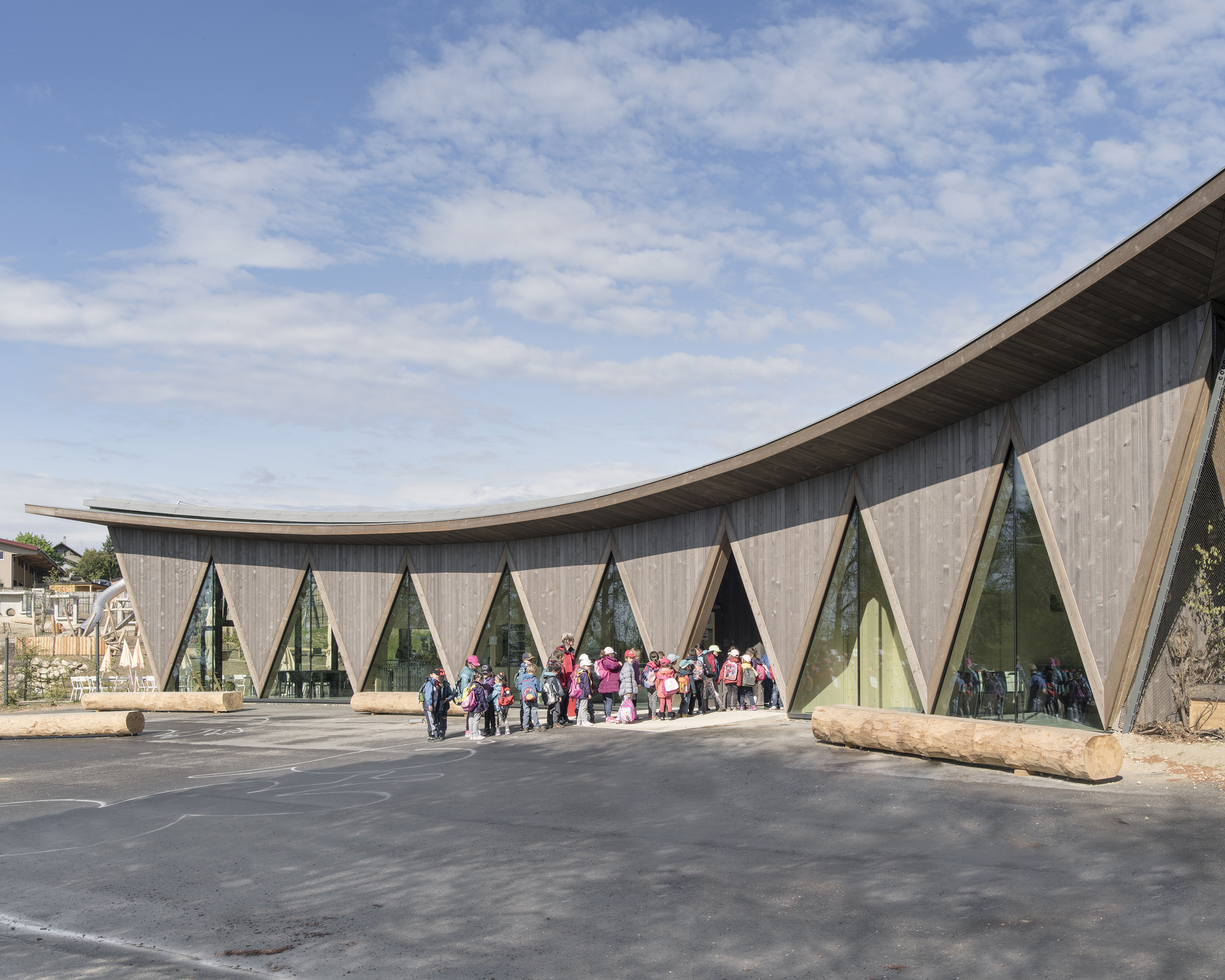 Deuxième Prix Région Ouest: Pavillon d’accueil du Parc Animalier de la Garenne, Le Vaud VD, 2016 Semblable aux volières en arrière-plan, la construction en bois incurvée s’insère dans le paysage et s’harmonise avec les autres unités qui l’entourent. La façade est constituée d’éléments triangulaires en bois, en équilibre sur la pointe. Cette forme singulière se lit tant à l’extérieur qu’à l’intérieur. Les cadres et les pleins composants ces triangles sont construits avec des