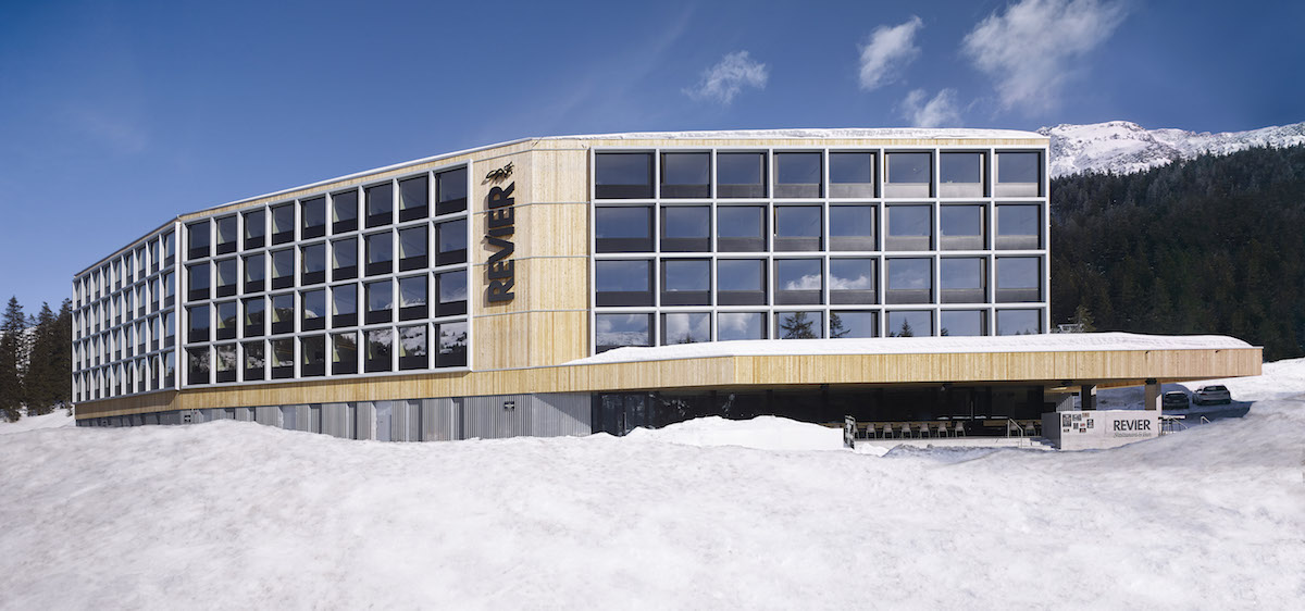An der Fassade der vier Zimmergeschosse sind die einzelnen Module mit hervorstehenden Metallzargen betont, ansonsten ist das Gebäude ein Holzbaukörper mit vertikaler Lattung aus unbehandelter Lärche.