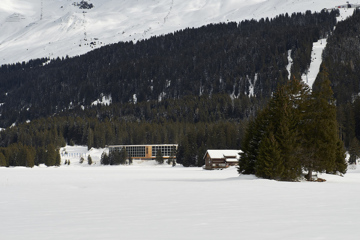 Einziges Schweizer Projekt: Das lange, schmale Gebäude der «Revier Mountain Lodge» in Lenzerheide steht an der steilen Geländekante des mächtigen Bergwalds im Hintergrund und folgt mit zwei leichten Knicken der Uferlinie des Heidsees.