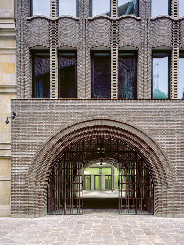 Welt der Steine: An der Nordseite des Baus führt ein Torbogen in den semi-öffentlichen Hof. An dieser Stelle treffen die neue Klinkerfassade, die schlicht gehaltene, weiss verputzte Hoffassade und die denkmalgeschützte Fassade des Altbaus aus Naturstein aufeinander.