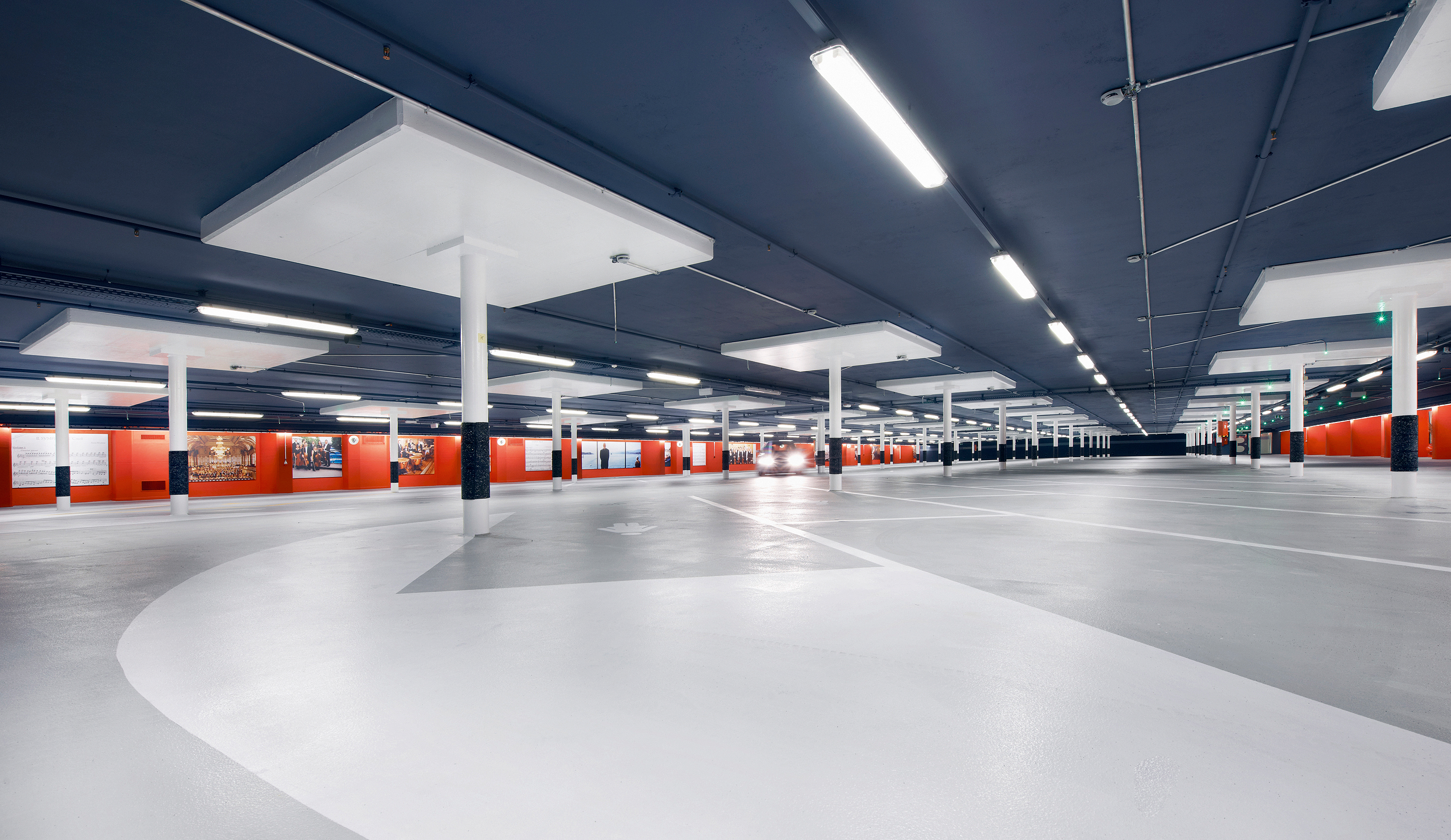 Beleuchtung und Farbkonzept unterstützen die durch den Umbau gewonnene Raumqualität der Parkgeschosse. Die Stützen mit ihren quadratischen Pilzen heben sich von der dunklen Decke ab, und eine tief hängende Beleuchtung erhellt die Pilzuntersicht