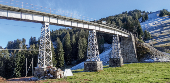 Brücke Unterstetten in genieteter Schweisseisenbauweise: Die über vier 12.5 m lange Felder durchlaufende Balkenbrücke hebt sich scharf von der Naturlandschaft ab. Die im Grundriss polygonal verlaufenden Vollwandträger mit untenliegendem horizontalem Wind­verband und mit Querträgern aus Diagonalkreuzen wirken statisch wie ein steifer Kastenträger, der die Biege- und Torsions­beanspruchungen aufnehmen kann.
