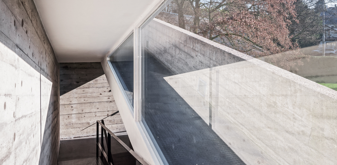Die betonierte Rampe führt auf der Nordfassade des Baus vom Erdgeschoss zur Dachterrasse. Sie bildet ebenso ein funktionales wie auch ein dokumentarisches Scharnier: als Erschliesssung und Verankerung am Ort und als Hinweis auf die ursprünglich geplante Materialisierung der Kuben.