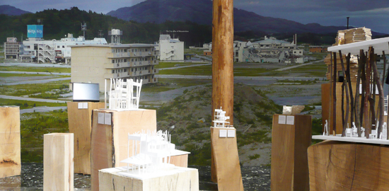 Die Ausstellung präsentiert an die Wand tapezierte Fotos der Gemeinde Rikuzentakata auf der Insel Honshu nach dem Tsunami 2011. Im Raum verteilt sind Modelle und Skizzen für die geplanten Wohnhäuser