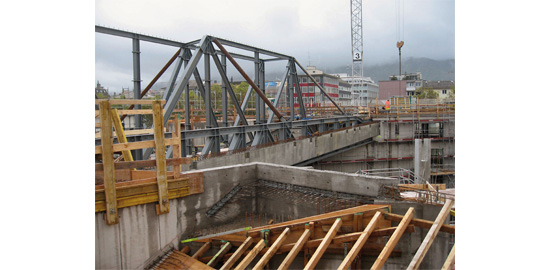 Impression de chantier?: la structure métallique du «?Pont habitable?» au-dessus de la sortie est de la halle des trams. Parallèlement, le premier porteur principal du toit de la halle en béton préfabriqué avec les niches pour l’appui de porteurs secondaires. A droite, le poteau intermédiaire pour le deuxième porteur principal. Au premier plan, le coffrage pour les escaliers.